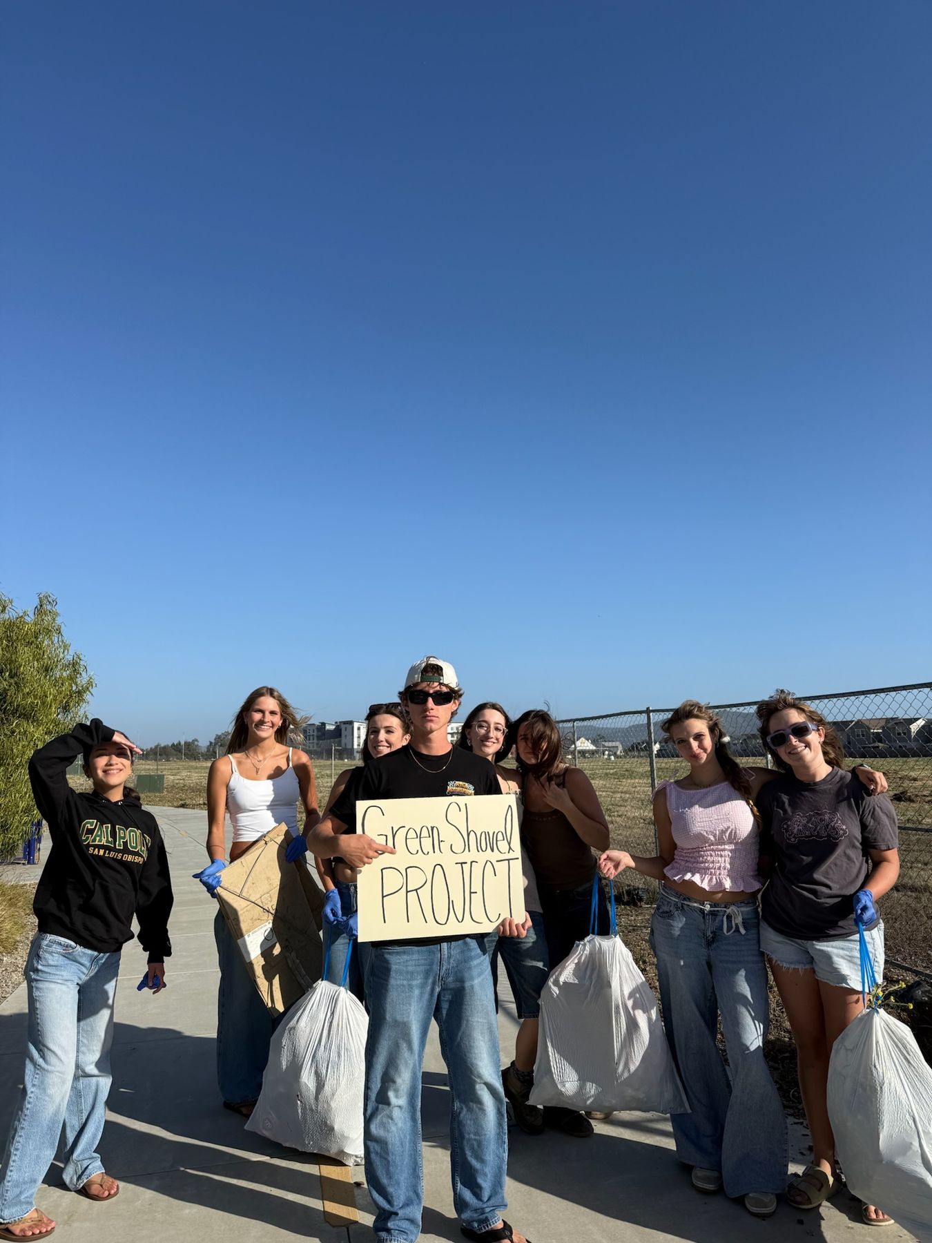 Volunteers in gloves on a paved path holding full trash bags and a Green Shovel Project sign